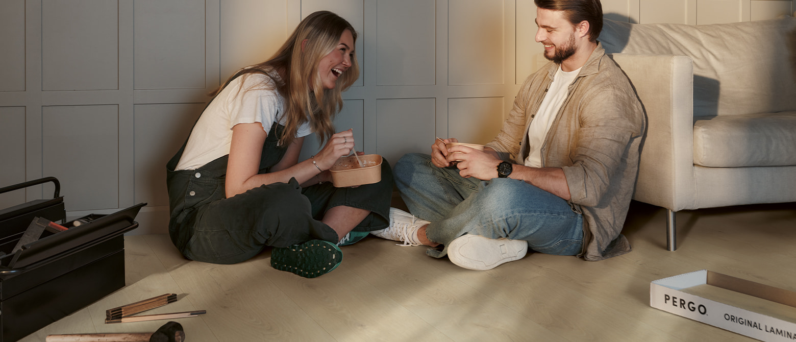 couple laughing and eating lunch on a beige laminate floor